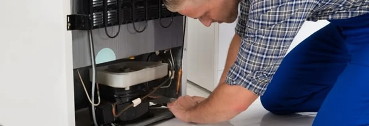 Refrigerator repair technician servicing the compressor and condenser area in Huntsville, AL